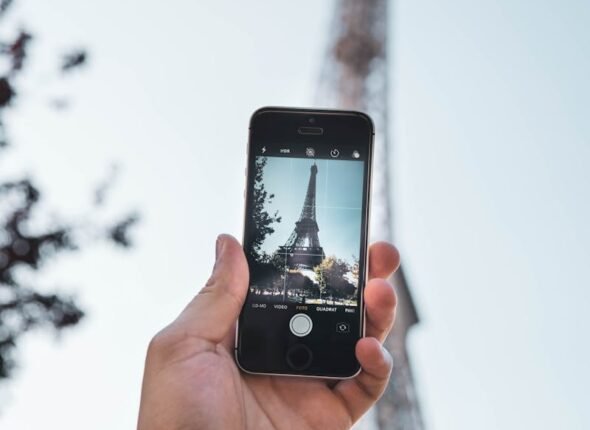 A person holds a smartphone to photograph the Eiffel Tower in Paris during daylight.